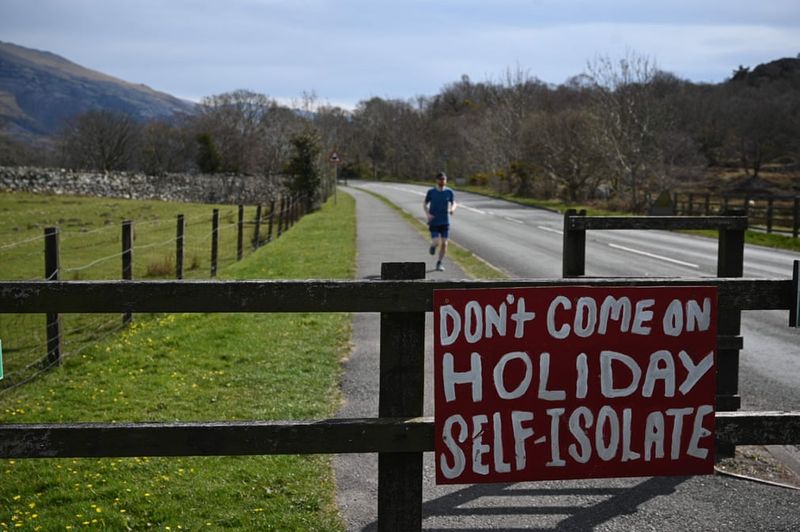Social distancing photos - sign saying don't come on holiday self isolate, with runner in the background