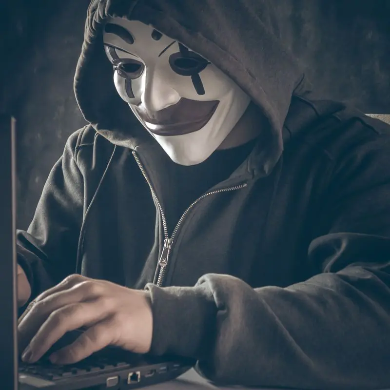 Coronavirus and Phishing - hacker with clown mask and hoodie in front of laptop