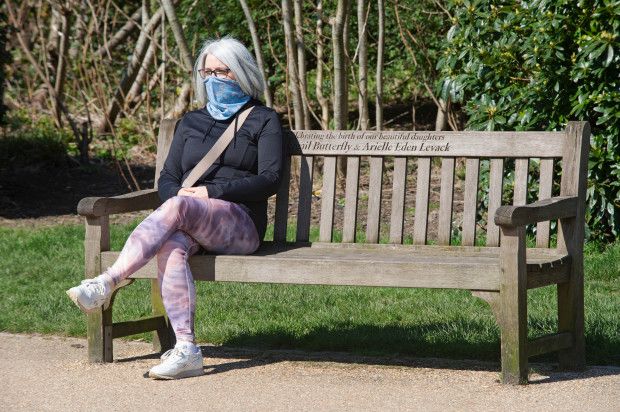 Social distancing photos - woman sitting on bench in the park wearing a mask