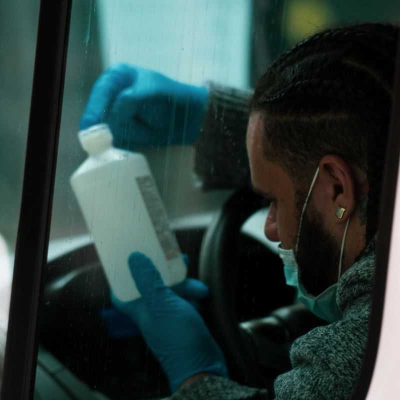 Coronavirus and Taxis - taxi driver with mask in the car looking at bottle of hand sanitiser