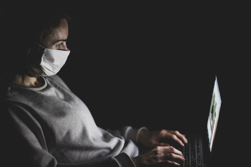 Coronavirus fake news - man wearing a face mask in front of her laptop in the dark